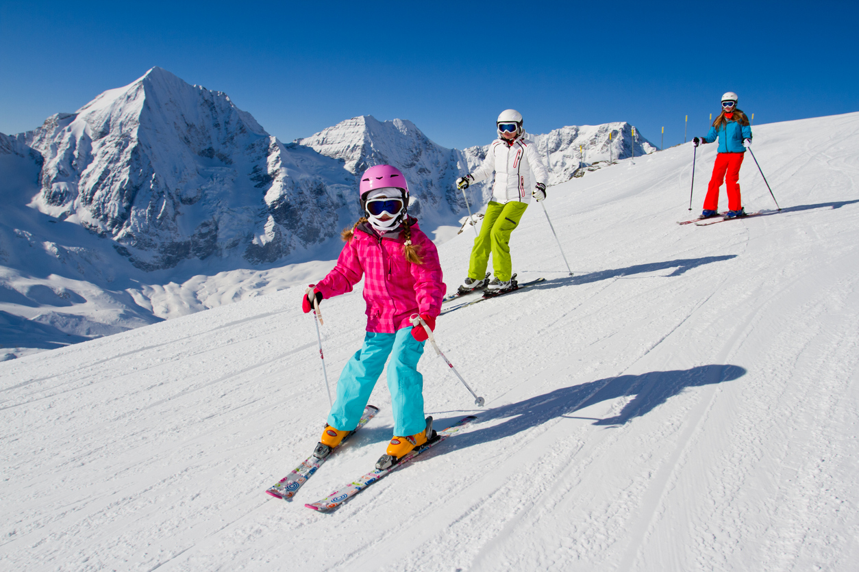 Young Family Skiing Down A Snowy Slope